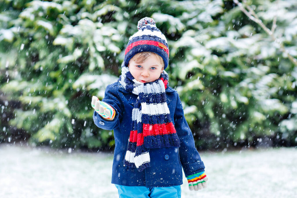 Lindo niño divertido en ropa de moda de invierno colorido divertirse y jugar con la nieve, al aire libre durante las nevadas. Activo ocio al aire libre con niños. Niño y niño cogiendo copos de nieve. - Foto, Imagen