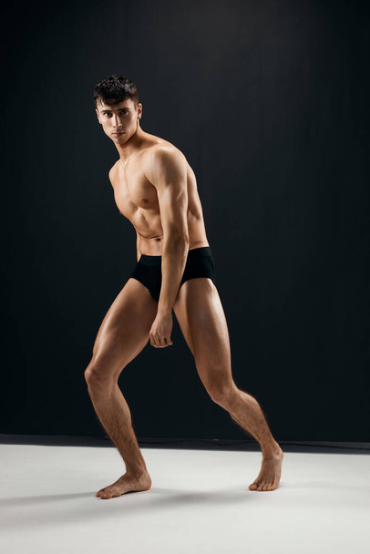 man with muscular naked body in black panties posing against dark background - Photo, Image