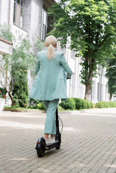 Back view of senior businesswoman riding electric kick scooter  - Foto, Imagen