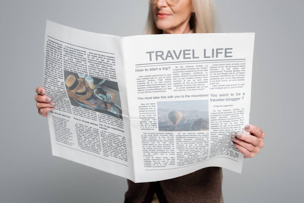 Ausgeschnittene Ansicht einer verschwommenen Seniorin, die Reisezeitung isoliert auf Grau hält  - Foto, Bild