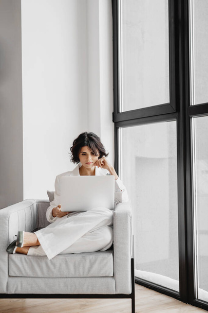 Young businesswoman sitting on chair with laptop near the window. - Zdjęcie, obraz