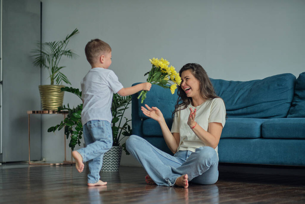 Счастливого Дня Матери. ребенок сын поздравляет мать с праздником и дарит цветы. поздравить ее с Днем матери во время праздника дома - Фото, изображение