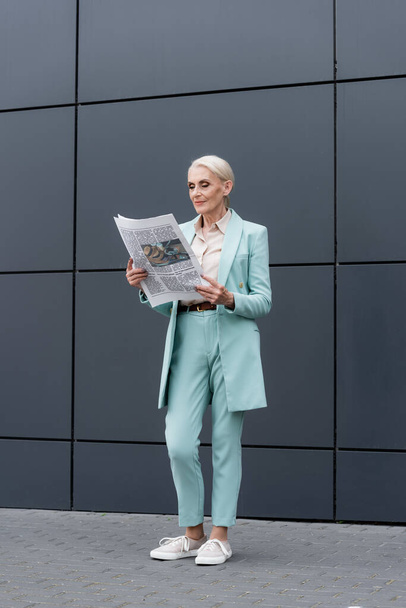 Mujer de negocios senior leyendo el periódico mientras está de pie cerca del edificio al aire libre  - Foto, imagen