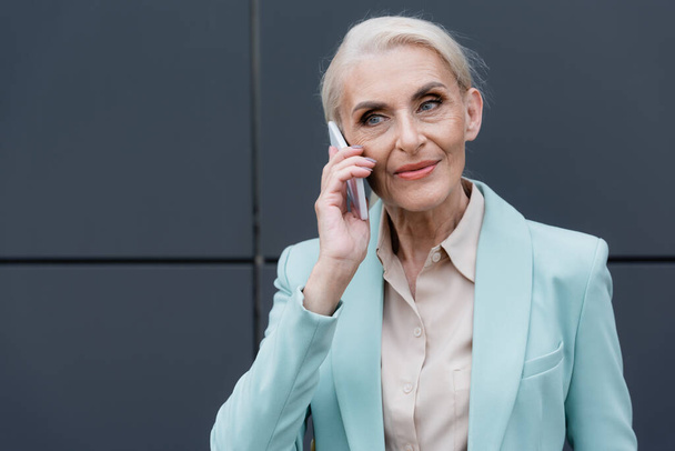 Elderly businesswoman talking on smartphone outdoors  - 写真・画像