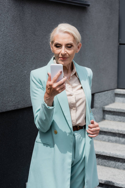 Elderly manager in formal wear using smartphone outdoors  - Foto, Imagem