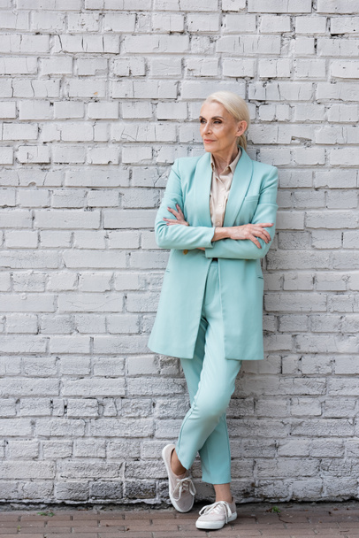 Elderly businesswoman standing with crossed arms near brick wall  - Foto, Bild