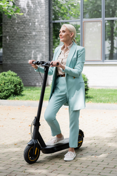 Seniorin steht mit Elektro-Tretroller auf Straße und schaut weg - Foto, Bild