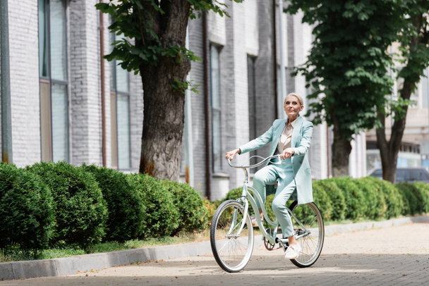 senior businesswoman in blue suit riding bicycle in city - Fotó, kép