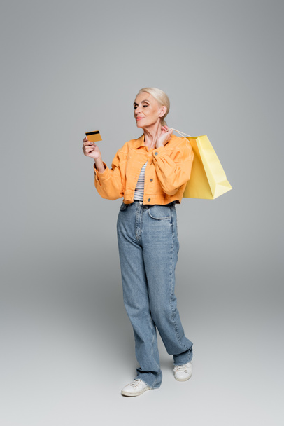 senior woman with shopping bags looking at credit card on grey - Фото, зображення