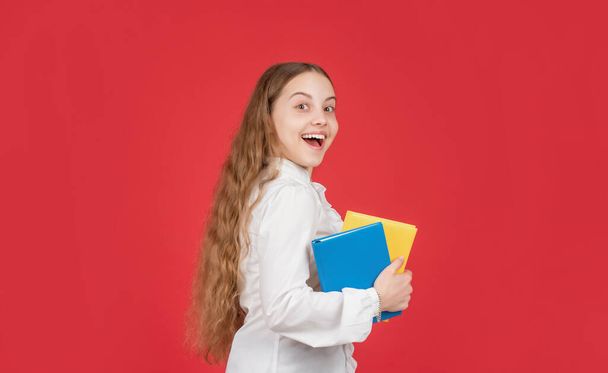 amazed teen girl in white shirt ready to study do homework with book on red background, education - Foto, Imagem