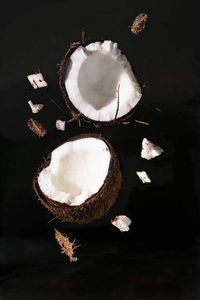 На темном фоне с твердым светом кокосовый орех разрезается пополам. вертикальная ориентация - Фото, изображение