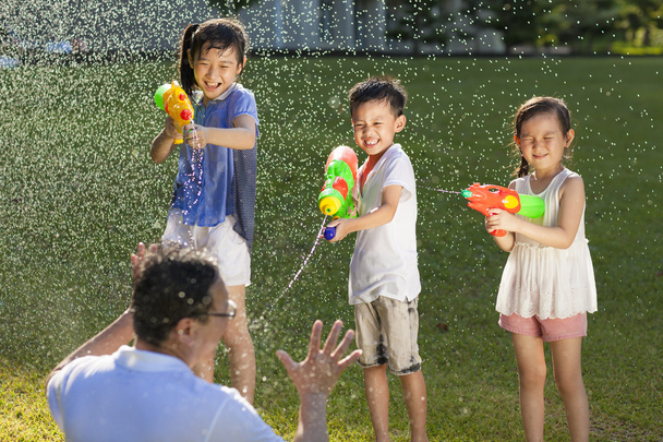 kleine jongens met behulp van water kanonnen te spuiten van hun vader - Foto, afbeelding