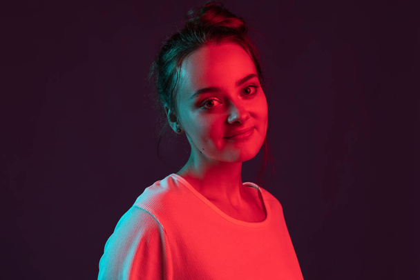 Close up portrait of sweet, pretty romantic girl on dark purple studio background in red neon light, filter. Concept of human emotions, facial expression. - Фото, изображение