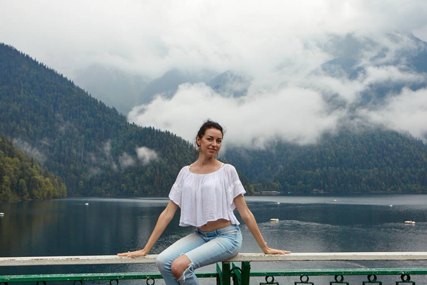 A girl in white clothing on a background of a mountain lake with blue water and mountains with clouds. Background. - Photo, Image