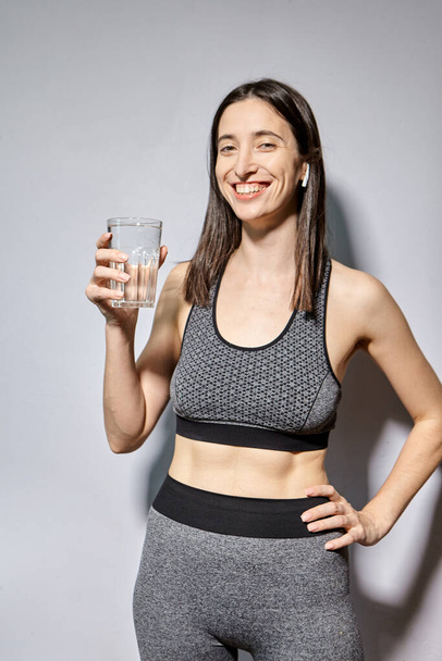 Una donna in abiti sportivi e con cuffie wireless beve acqua. il concetto di uno stile di vita sano e di attività sportive - Foto, immagini