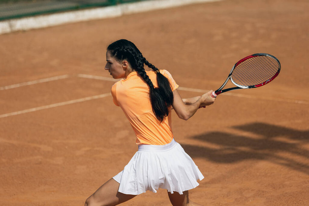 Uma bela jovem esportista, tenista profissional com raquete praticando em quadra de tênis de barro no dia de verão. - Foto, Imagem