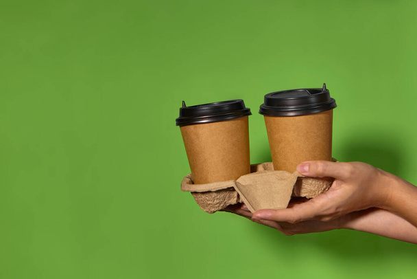 Großaufnahme auf grünem Hintergrund, Frauenhände halten zwei Pappbecher mit Kaffee in einem Ständer. Kaffee oder Tee mit Ihnen. Aktion zwei zum Preis von einem, Kaffee-Lieferung. - Foto, Bild