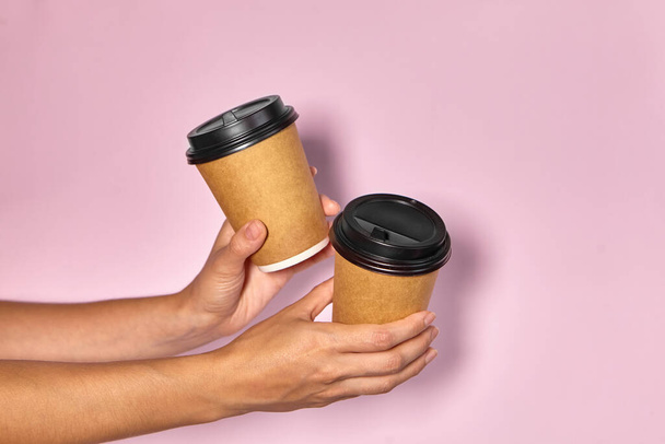 Vaaleanpunaisella pohjalla lähikuva, naisen käsi pitää paperimukia, jossa on kahvia jalustalla. Kahvia tai teetä mukaan. Ihmiset ojentavat toisilleen kupin kahvia, kahvin toimituksen. - Valokuva, kuva