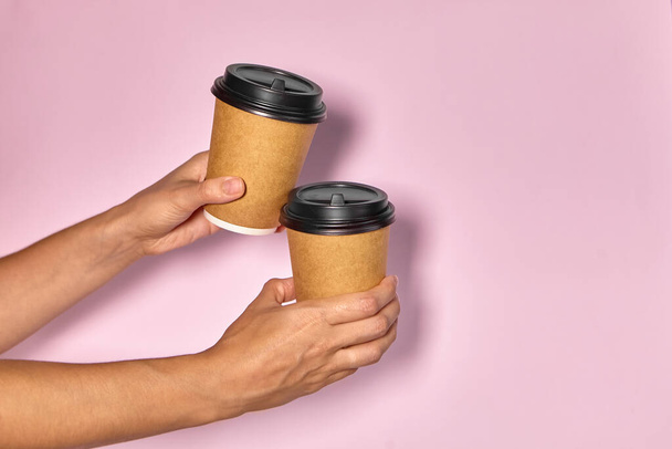 Κοντινό πλάνο σε ροζ φόντο, το χέρι μιας γυναίκας κρατά ένα χάρτινο κύπελλο με καφέ σε ένα περίπτερο. Καφέ ή τσάι για έξω. Ο κόσμος πασάρει ο ένας στον άλλο καφέ, παράδοση καφέ.. - Φωτογραφία, εικόνα