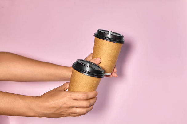 Close-up on a pink background, a woman's hand holds a paper cup with coffee in a stand. Coffee or tea to go. People hands passing one another cup of coffee, coffee delivery. - 写真・画像