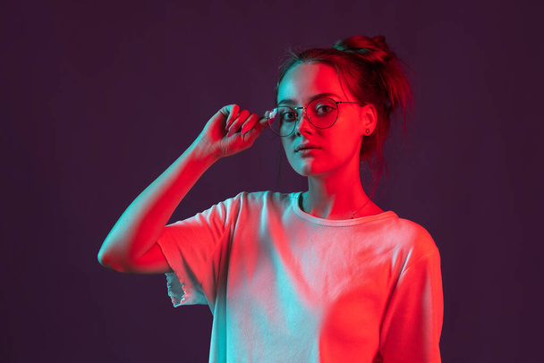 Portrait of beautiful girl in casual clothes isolated on dark purple studio background in red neon light, filter. Concept of human emotions, facial expression. - Foto, Bild