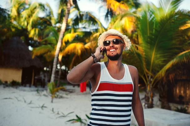 Handsome tourist man talking on smartphone against background of palm trees - Fotó, kép