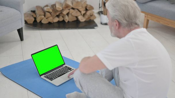 Viejo usando el ordenador portátil con la pantalla verde en la estera del ejercicio - Foto, imagen
