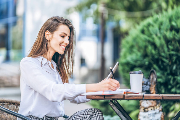 Young business woman drinking coffe and working on tablet in street cafe - Фото, зображення