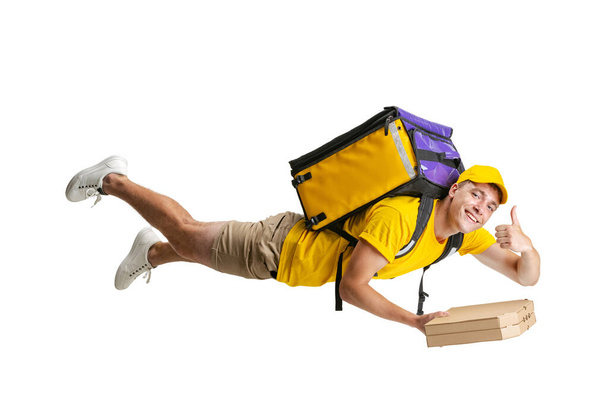 Young delivery man in yellow uniform flying to deliver order isolated on white background. Concept of convenience, speed, comfort, safety, service. - Foto, Imagen
