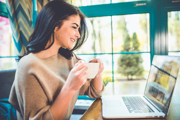 Привлекательная женщина с ноутбуком пьет кофе в кафе - Фото, изображение