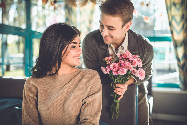 Ο ευτυχισμένος άντρας δίνει λουλούδια σε μια γυναίκα στο εστιατόριο. - Φωτογραφία, εικόνα
