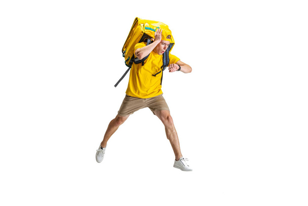 Young delivery man in yellow uniform running to deliver order isolated on white background. Concept of convenience, speed, comfort, safety, service. - Φωτογραφία, εικόνα