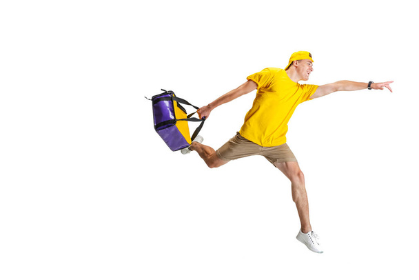 Young delivery man in yellow uniform hurry up to deliver order isolated on white background. Concept of convenience, speed, comfort, safety, service. - Φωτογραφία, εικόνα