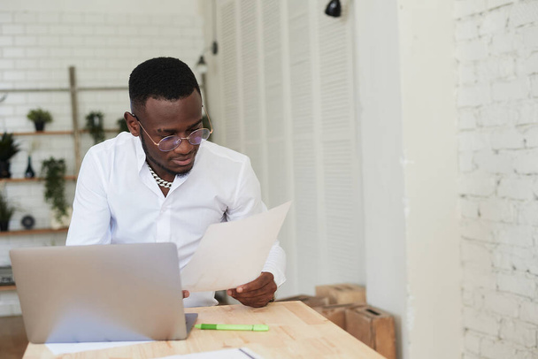 Heureux homme afro-américain concentré faisant un appel vidéo avec des partenaires clients. Jeune homme noir utilise un ordinateur portable dans un bureau moderne - Photo, image