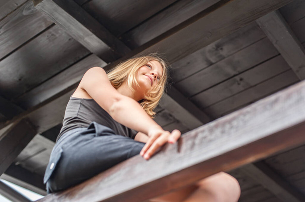 Retrato de una hermosa adolescente sentada en una valla de madera y mirando a la distancia - Foto, Imagen