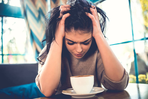 A stresszes nő egy csésze kávéval ül a kávézóban. - Fotó, kép