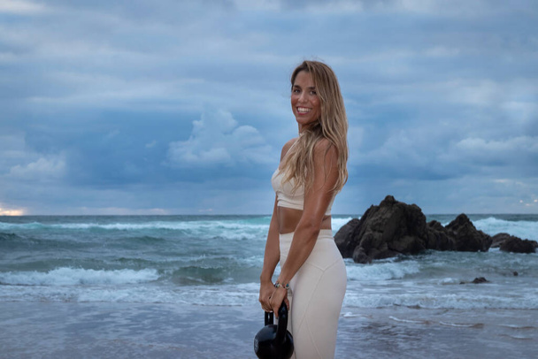 nuori blondi nainen käyttää meren rannalla vedenkeitin kanssa - Valokuva, kuva