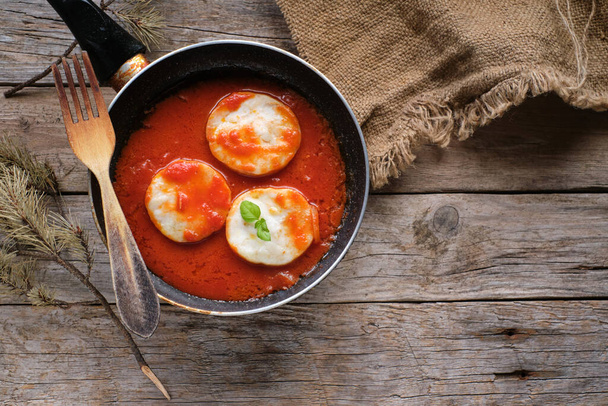 Hake medallions with tomato in a frying pan on rustic wooden table - Фото, изображение