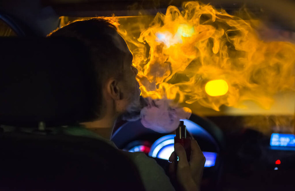 The man smoke an electrical cigarette in the car. Evening night time - Foto, Imagen