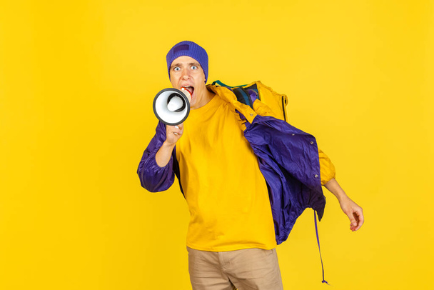 Comic portrait of young man, delivery guy in uniform isolated on yellow studio background. Concept of humor, safety, service. Complementary colors - Zdjęcie, obraz