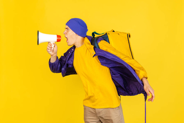 Comic portrait of young man, delivery guy in uniform isolated on yellow studio background. Concept of humor, safety, service. Complementary colors - Фото, изображение