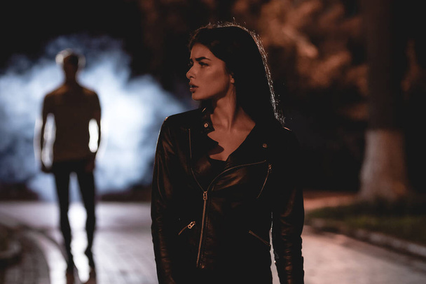 Kadın dumanlı bir adamın arka planında karanlık bir sokakta duruyor. Gece vakti. - Fotoğraf, Görsel