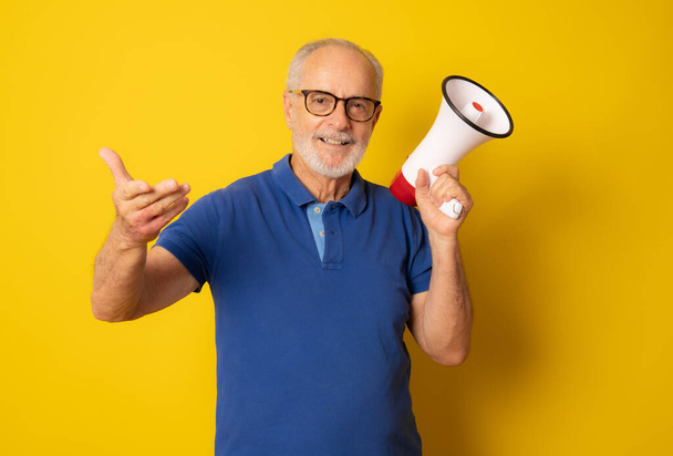 Senior smiling man with megaphone isolated over yellow background. - Photo, Image