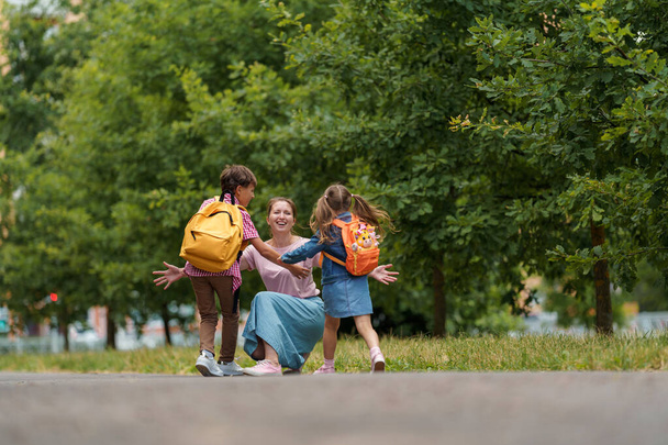 loving family. caring mother meets cheerful children, boy and girl with backpacks running in her arms, meeting children hugging them, after school classes in park. Back to school. first day training - Foto, Imagem