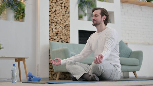 Genç adam evde egzersiz üzerine meditasyon yapıyor. - Fotoğraf, Görsel