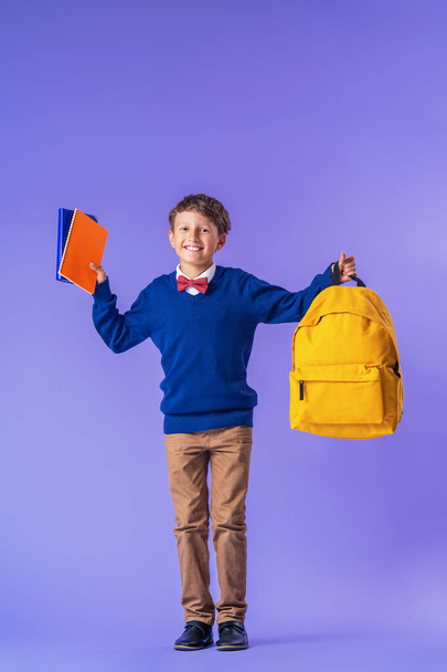 cheerful mischievous schoolboy in uniform with a backpack jumps on a purple background. Dynamic images that go back to the school concept. beginning of holidays. Back to school. boy is ready to study. - Фото, зображення