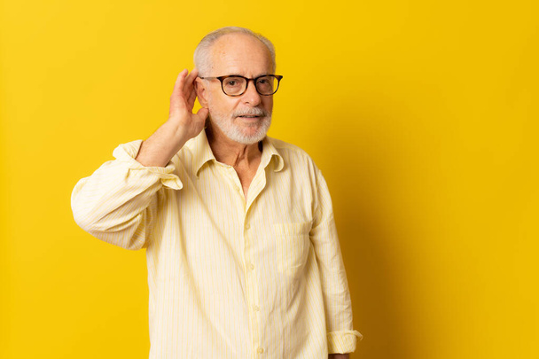 Kıdemli yaşlı adam sarı arka planda dinleme hareketi yapıyor.. - Fotoğraf, Görsel
