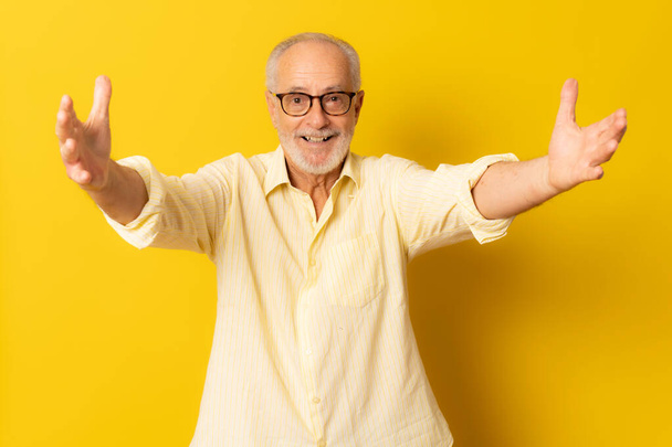 Hombre mayor dando un abrazo a la cámara sobre fondo amarillo. - Foto, imagen