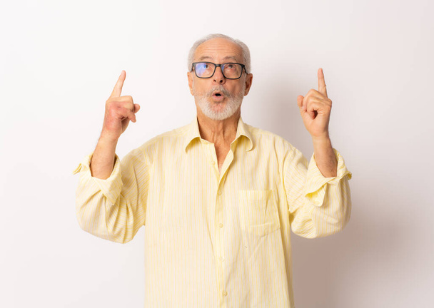 Senior überrascht Mann zeigt mit dem Finger nach oben über weißen Hintergrund. - Foto, Bild