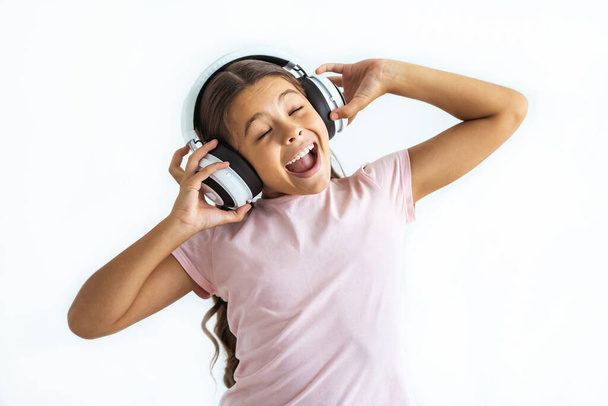 Το χαρούμενο κορίτσι που ακούει μουσική με ακουστικά στο φόντο του λευκού τοίχου - Φωτογραφία, εικόνα